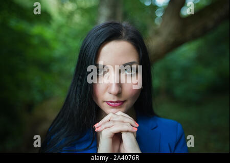 Ein Mädchen betet für die Natur. Im Freien. Brünette mit ausdrucksvollen Augen, Hände, Blick in die Kamera. In einem blauen Anzug vor dem Hintergrund o Stockfoto