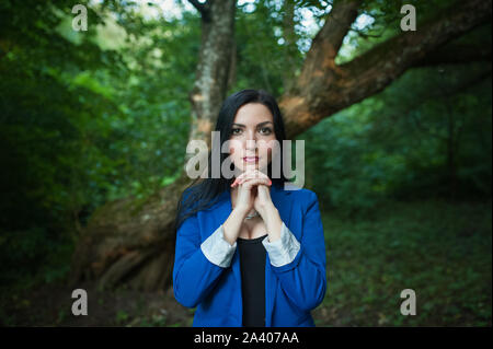 Ein Mädchen betet für die Natur. Im Freien. Brünette mit ausdrucksvollen Augen, Hände, Blick in die Kamera. In einem blauen Anzug vor dem Hintergrund o Stockfoto