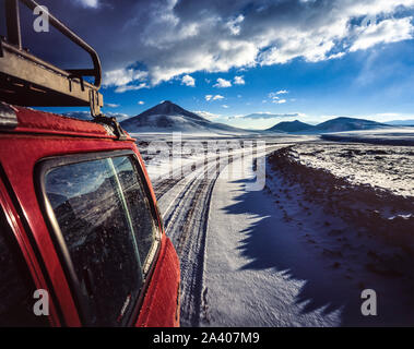 Rot Jeep entlang einer Schnee-Pfad auf dem Altiplano in Bolivien, mit Bergen im Hintergrund Stockfoto