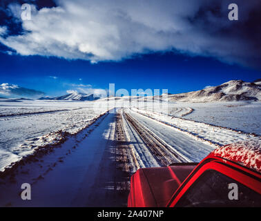 Rot Jeep entlang einer Schnee-Pfad auf dem Altiplano in Bolivien, mit Bergen im Hintergrund Stockfoto