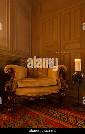 Wohnzimmer mit antiken eleganten beigen Sessel. Weihnachten am Abend bei Kerzenschein. klassische Wohnungen mit Kamin, geschmückten Baum, Sessel. Stockfoto