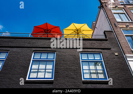 Die roten und gelben Sonnenschirmen auf einem hohen Balkon gegen den blauen vor weißen und blauen Fenstern Stockfoto