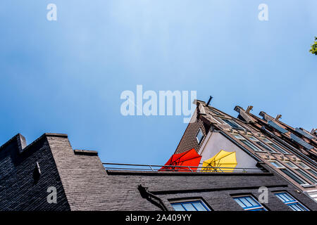 Die roten und gelben Sonnenschirmen auf einem hohen Balkon gegen den blauen Himmel und ein Flugzeug fliegen über echten High Stockfoto