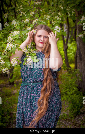 Porträt von einem schönen Mädchen in den Blumen. Ein Plus size model Posen auf dem Hintergrund der blühenden Kirschbaum. Stockfoto
