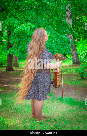 Das Konzept der Inspiration. Schöne Mädchen mit langen Haaren hält eine Violine in den Händen. Volle Mädchen in vollem Wachstum.? Stockfoto