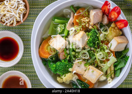 Vegetarische vietnamesische Nudelsuppe Pho diente in Weiße, runde Schüssel, mit Saucen, Kalk, Chili und Sojasprossen. Ansicht von oben. Stockfoto