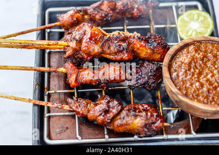 Sate Ayam gegrillte Hähnchen Fleisch auf Holzspieße mit Sambal kacang - Erdnuss Soße. Auf einem keramischen Holzkohle Grill serviert. Stockfoto