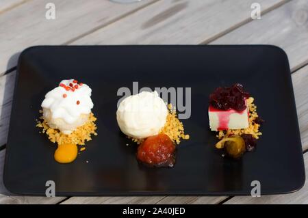 Satz von verschiedenen Desserts mit Früchten, Mousse, Kekse auf schwarzem Teller. Stockfoto