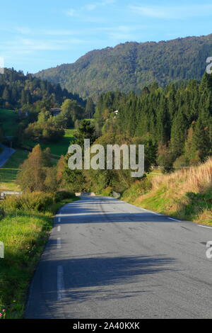 Eine geteerte Landstraße verläuft durch die ländliche Landschaft auf der Insel Osterøy im Kreis Vestland, Norwegen. Stockfoto