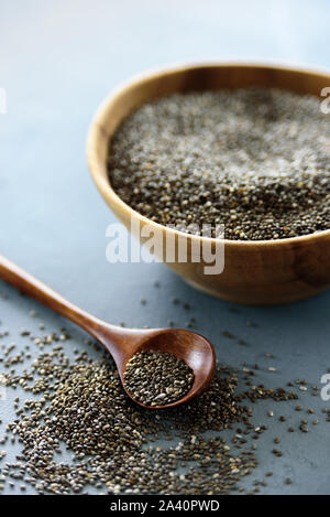Chia Samen in alte hölzerne Schüssel mit Löffel aus Holz auf blauem Hintergrund Stockfoto