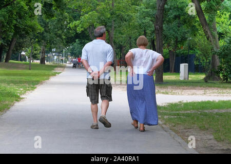 Ältere Paare ist Wandern in Green City Park auf Urlaub. Paar mittleren Alters. Bäume auf den Seiten von Trail. Sonnig warmen Tag. Stockfoto