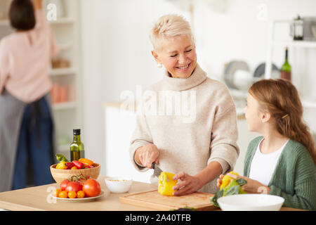Gerne schöne Großmutter Schneiden von Gemüse und lächelnd zu ihrer Enkelin, die ihr hilft in der Küche zu kochen Stockfoto