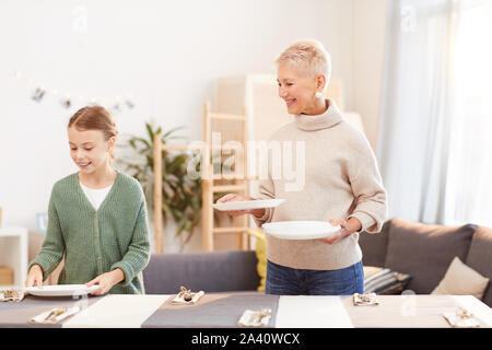 Lächelnd reife Mutter die Teller auf dem Tisch mit ihrer Tochter hilft Ihr im Wohnzimmer zu Hause. Stockfoto