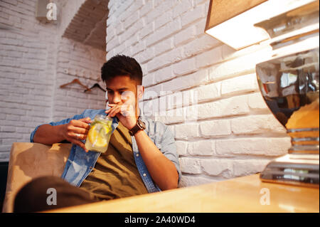 Portrait von Stattlichen erfolgreiche bärtigen Südasiatischen, jungen indischen Freelancer in Blue Jeans Shirt im Cafe sitzen mit Limonade. Stockfoto