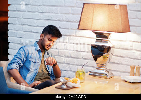 Portrait von Stattlichen erfolgreiche bärtigen Südasiatischen, jungen indischen Freelancer in Blue Jeans Shirt im Cafe mit Chicken Nuggets und Limonade sitzen. Stockfoto