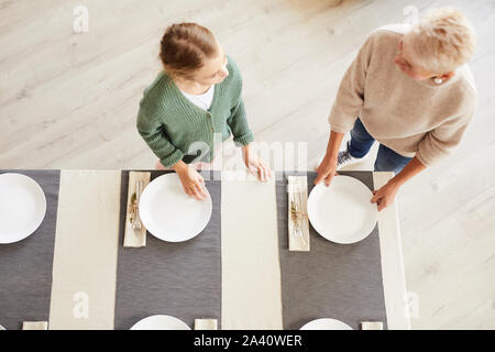 Hohe Betrachtungswinkel von Mutter Einstellung der Tabelle und ihrer Tochter helfen, ihr vor dem Abendessen mit der Familie zu Hause. Stockfoto