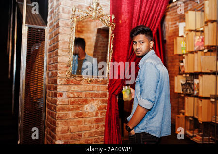 Portrait von Stattlichen erfolgreiche bärtigen Südasiatischen, jungen indischen Freelancer in Blue Jeans Shirt im Cafe mit Cocktail gegen den Spiegel. Stockfoto