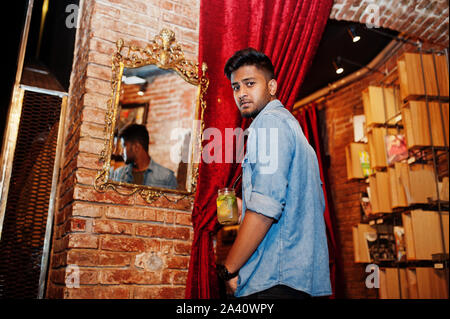 Portrait von Stattlichen erfolgreiche bärtigen Südasiatischen, jungen indischen Freelancer in Blue Jeans Shirt im Cafe mit Cocktail gegen den Spiegel. Stockfoto