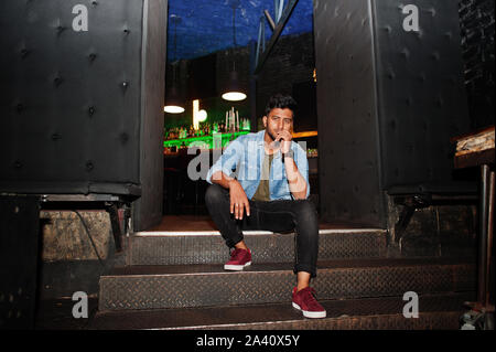 Portrait von Stattlichen erfolgreiche bärtigen Südasiatischen, jungen indischen Freelancer in Blue Jeans Shirt im Night Club stehen. Stockfoto