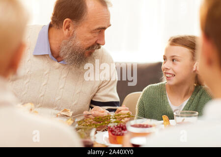 Älterer Mann mit Bart im Gespräch mit seiner Enkelin, während Sie Essen am Tisch beim Abendessen mit der Familie Stockfoto