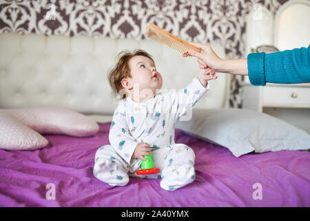 Mom combes ein kleines Kind. Mutter hand Putzen mit einem Kamm seine adorable Baby Haar, Mutter kümmert sich um Kind. selektive Fokus Stockfoto