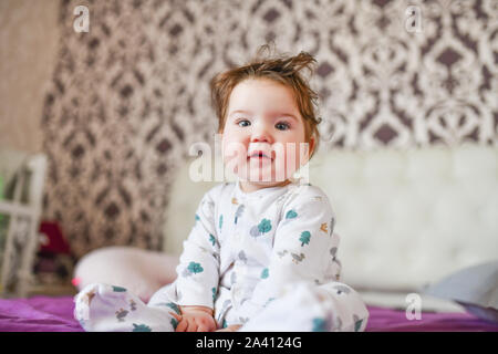 Baby auf Kamera posiert auf dem Bett zu sitzen. Das Kind spielt in Betten. Stockfoto