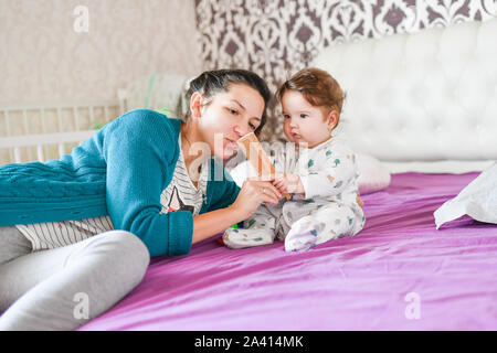 Mama spielt mit dem Baby auf dem Bett. Mama spielt mit Baby im Zimmer im Innenbereich. Mama spielt mit dem Baby im Zimmer im Innenbereich Stockfoto
