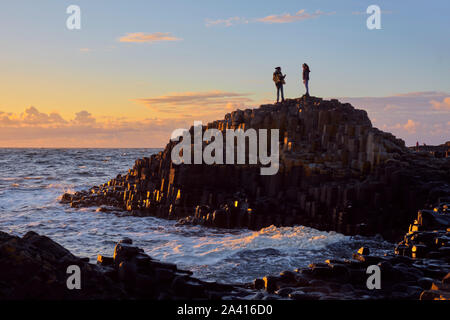 Silhouette von zwei Leute an der Giant's Causeway Felsen bei Sonnenuntergang in Nordirland stehen Stockfoto