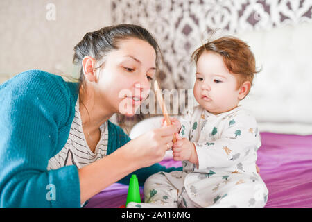 Mama spielt mit dem Baby auf dem Bett. Mama spielt mit Baby im Zimmer im Innenbereich. Mama spielt mit dem Baby im Zimmer im Innenbereich Stockfoto