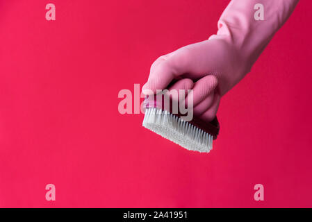 Hand in Rosa latex Schutzhandschuh mit Staub Pinsel auf rosa Hintergrund. Reinigung und Hausarbeit arbeiten Konzept Stockfoto