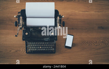 Vintage Schreibmaschine mit Smartphone auf hölzernen Tisch. Business, Technologie Fortschritt Konzept Stockfoto