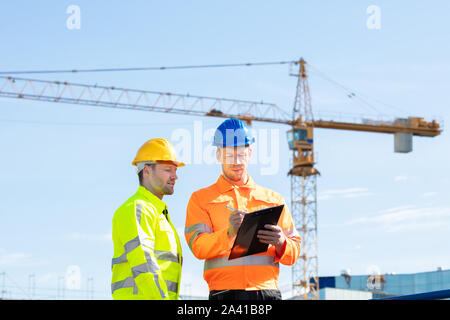 Männliche Architekten erteilen Anweisungen an seine Vorarbeiter auf Zwischenablage Arbeiten auf der Baustelle Stockfoto