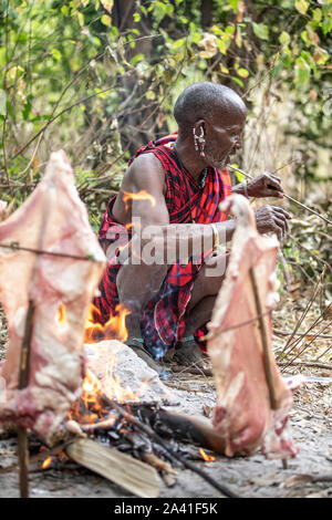 Arusha, Tansania, 7. September 2019: Masai Mann kochen Fleisch auf Feuer Stockfoto