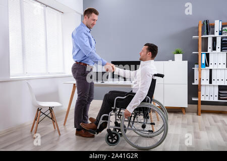 Zuversichtlich, dass junge Unternehmer Sitzen im Rollstuhl zitternden Hand mit männlichen Kollegen Im modularen Office Stockfoto