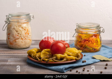 Hausgemachte eingelegte Paprika und Tomaten auf einer Keramikplatte auf einer Leinwand Serviette. Neben Gläser Sauerkraut. Im rustikalen Stil Stockfoto