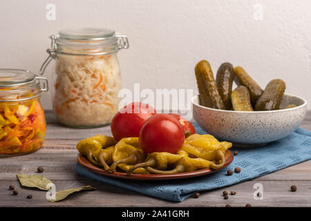 Hausgemachte eingelegte Paprika und Tomaten auf einer Keramikplatte auf einer Leinwand Serviette. Neben Pickles in einer Salatschüssel und Gläser Sauerkraut. Im rustikalen Stil Stockfoto