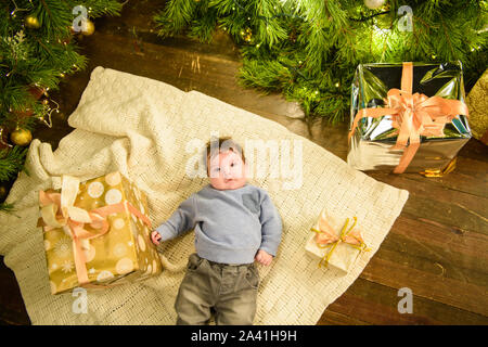 Kind in der Nähe von Weihnachten Baum Ansicht von oben. Closeup Portrait von lächelnden niedlichen Kind im Urlaub Weihnachten Innenraum in der Nähe der Festliche Baum. Blick von oben auf die Happy Stockfoto