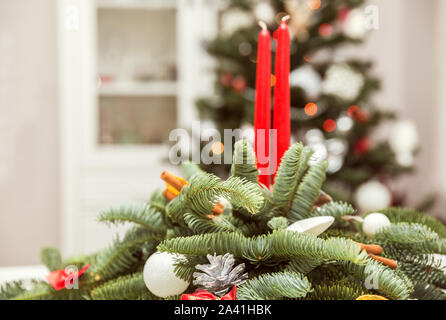 Weihnachten Dekorationen mit Kerzen. Tannenzweigen mit Kugeln, Kegel und zwei rote Kerzen im Innenraum mit einem Weihnachtsbaum Stockfoto