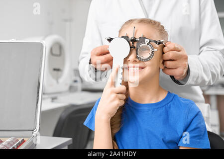 Lächelnde Mädchen in speziellen glassses mit Linse die Buchstaben auf der Suche und Überprüfung der Vision in optischen Speichern. Hübsches Kind schließen Auge und lächelnd in der Klinik. Kleines Mädchen Verbesserung der Augen. Konzept der Gesundheit. Stockfoto
