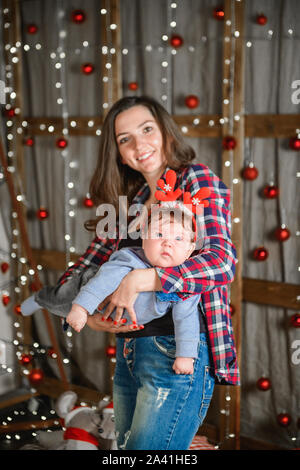 Mama und Baby Umarmung am Weihnachtsbaum. Happy Baby und seine Mutter sind auf den Rahmen. Mama mit Sohn umarmen für Weihnachten. und Spaß haben. Neugeborene Stockfoto