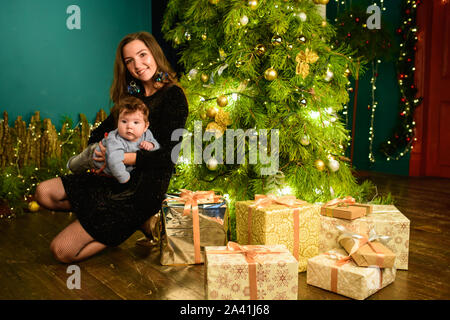 Mama und Baby Umarmung am Weihnachtsbaum. Happy Baby und seine Mutter sind auf den Rahmen. Mama mit Sohn umarmen für Weihnachten. und Spaß haben. Neugeborene Stockfoto