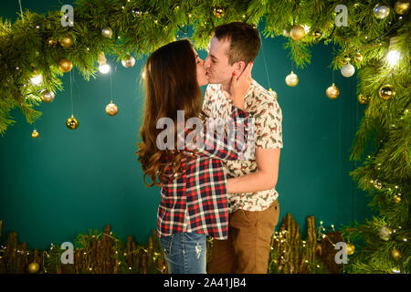 Verliebtes Paar in der Nähe von Weihnachten Hintergrund. Junges Paar Küssen in der Nähe der Weihnachtsbaum. Low Key. Silhouette Stockfoto