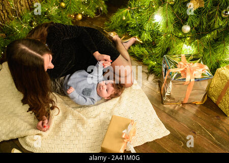 Mama und Baby Umarmung am Weihnachtsbaum. Happy Baby und seine Mutter sind auf den Rahmen. Mama mit Sohn umarmen für Weihnachten. und Spaß haben. Neugeborene Stockfoto