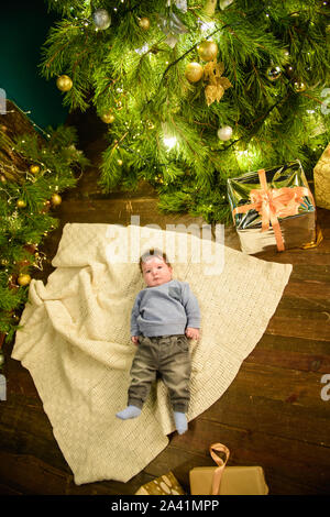 Kind in der Nähe von Weihnachten Baum Ansicht von oben. Closeup Portrait von lächelnden niedlichen Kind im Urlaub Weihnachten Innenraum in der Nähe der Festliche Baum. Blick von oben auf die Happy Stockfoto