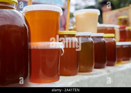 Eine Menge Gläser mit verschiedenen Arten von Honig auf dem Markt. Gesund selbstgemachte Produkt auf dem Tisch. Gelbe, orange und braune Flüssigkeiten. Geschäfte der beeke Stockfoto