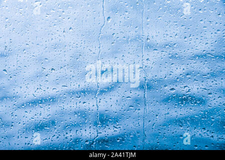 Wasser fällt auf Glas vor blauem Hintergrund ab Stockfoto