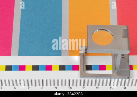 Silber Lupe stehend auf dem Testdruck, farbigen Hintergrund. Drucken Lupe auf Offset gedrucktes Blatt mit grundlegenden Farben- und Symbolleisten. Stockfoto