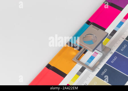 Silber Lupe stehend auf dem Testdruck, farbigen Hintergrund. Drucken Lupe auf Offset gedrucktes Blatt mit grundlegenden Farben- und Symbolleisten. Stockfoto