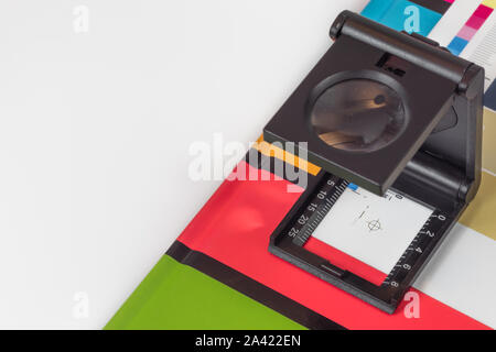 Schwarz Lupe stehend auf dem Testdruck mit farbigen Hintergrund. Drucken Lupe auf Offset gedrucktes Blatt mit grundlegenden Farben- und Symbolleisten. Stockfoto