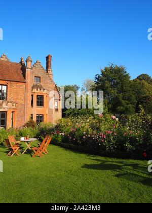 Chenies Manor House an einem spätsommerabend vor blauem Himmel mit Cosmos, Dahlien und Cleome mit schleichender Schatten auf dem Rasen. Stockfoto